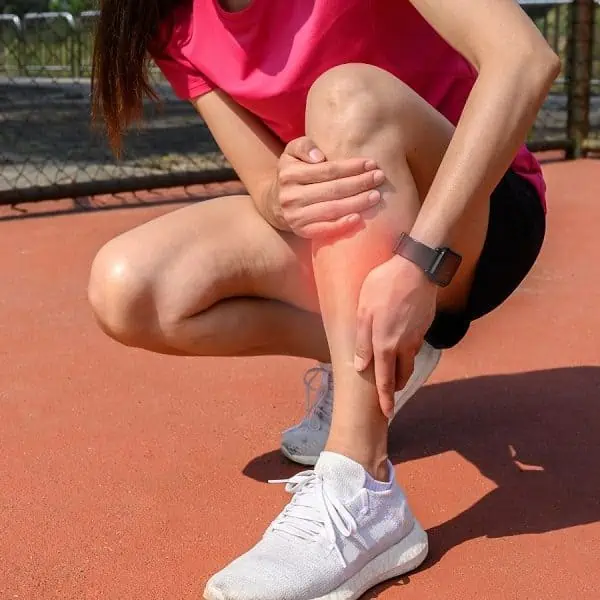 Señora sosteniendo la parte inferior de la pierna con dolor en la espinilla